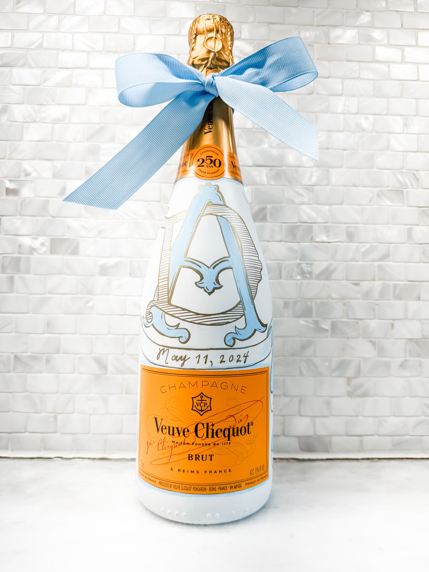 hand painted champagne bottle veuve cliquot bottle decorated in blue and white with monogram initials and the church painted on back with the wedding date and bride and groom's name with a blue grosgrain ribbon on top custom bottle bespoke and personalized